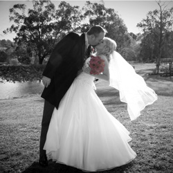 Nicole & Brett kissing at wedding with pink gerberas